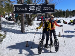 「北八ヶ岳 坪庭 2237m」の看板の前で、スノーシューを履いた参加者
